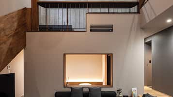 A modern interior with a large seating area, a staircase, and a high ceiling with recessed lighting.