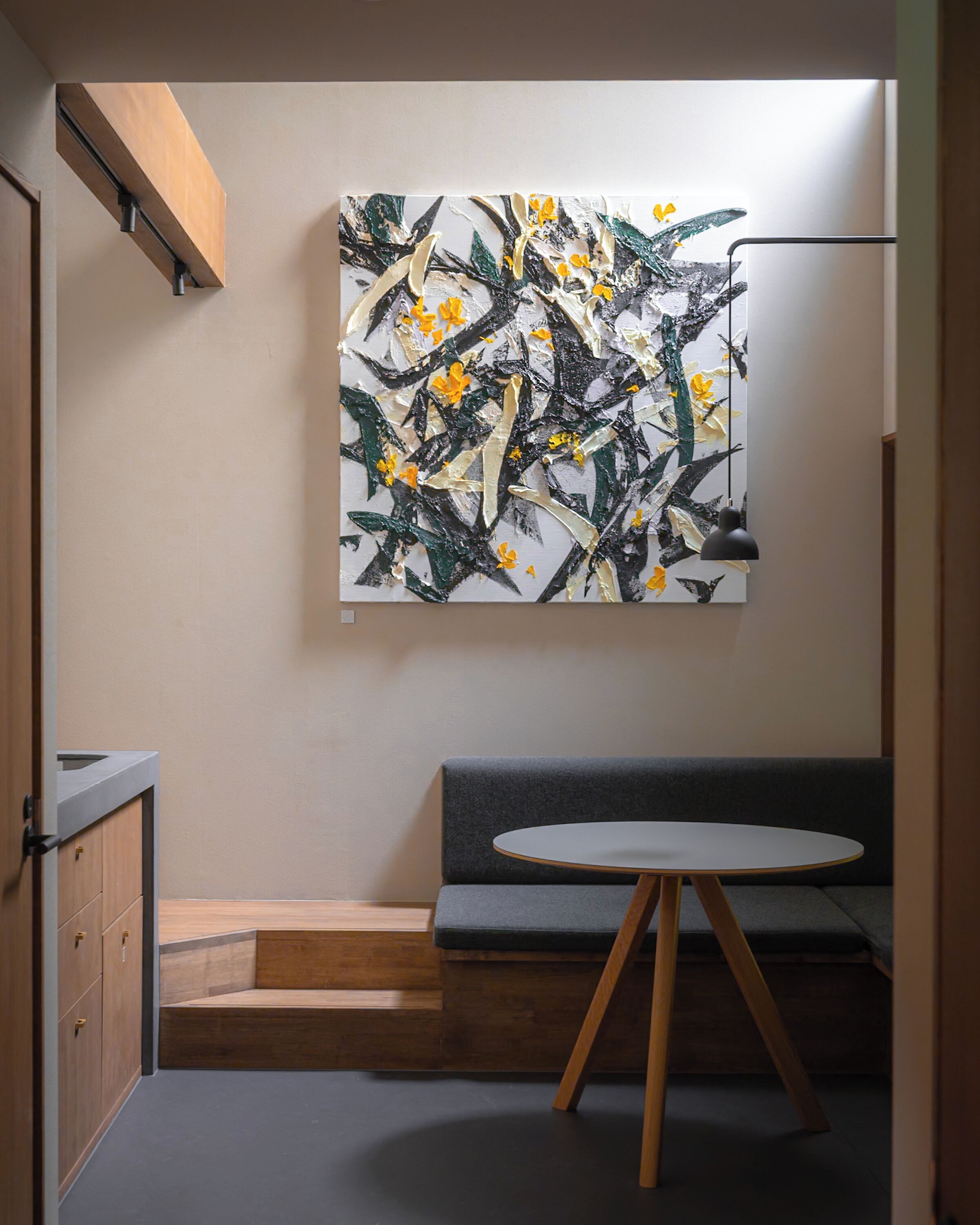 Un interior moderno con diseño minimalista, que incluye un armario de madera, un sofá gris, una mesa redonda y un cuadro abstracto colgado en la pared.