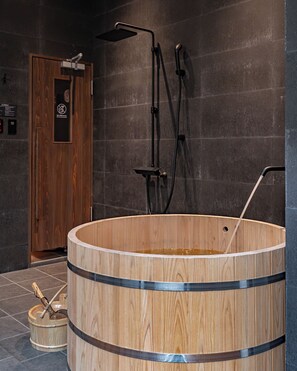 Een houten jacuzzi met douchekop en slang, een houten deur en een betegelde vloer.