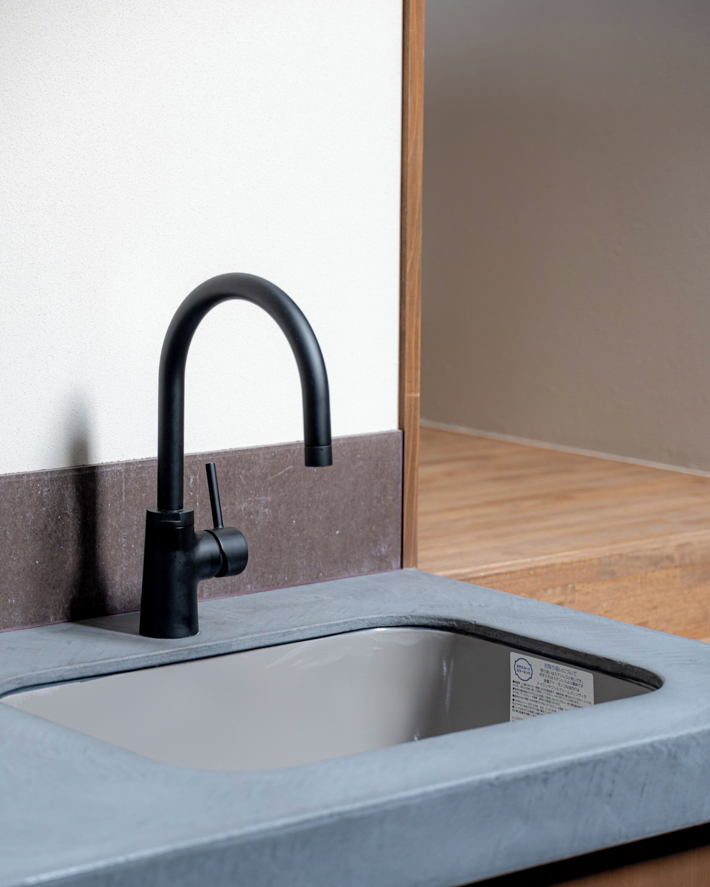 A modern kitchen sink with a curved faucet, a marble countertop, and a wooden floor.