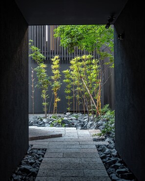 A narrow stone pathway leading to a garden with bamboo plants and a wooden fence. - TOVILLA STAY Niigata Honcho (Niigata-shi, Chuo-ku)