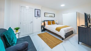 A hotel room with a bed, a desk, a chair, a small table with a plant, and a door. - Elegant 1BR Heathrow Direct West Kensington (London)