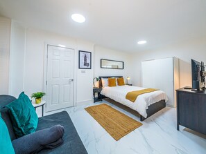 A hotel room with a bed, a desk, a chair, a small table with a plant, and a door. - Elegant 1BR Heathrow Direct West Kensington (London)