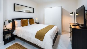 A hotel room with a bed, bedside lamps, a television, a wardrobe, and a mirror on the wall. - Elegant 1BR Heathrow Direct West Kensington (London)