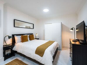 A hotel room with a bed, bedside lamps, a television, a wardrobe, and a mirror on the wall. - Elegant 1BR Heathrow Direct West Kensington (London)