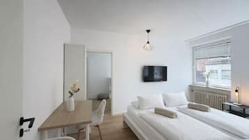 A modern bedroom with a bed, bedside table, chair, and a TV mounted on the wall.