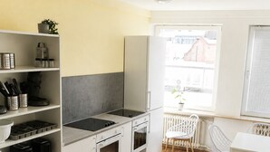 Una cocina compacta con armarios blancos, una estufa empotrada y una zona de comedor con sillas y una mesa blancos.