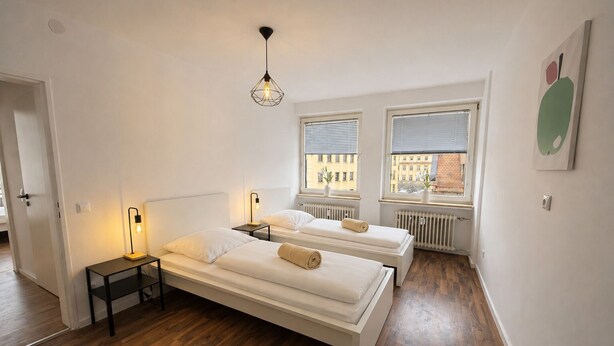 Habitación con dos camas, una lámpara de pie, luz de techo y ventana con persianas.