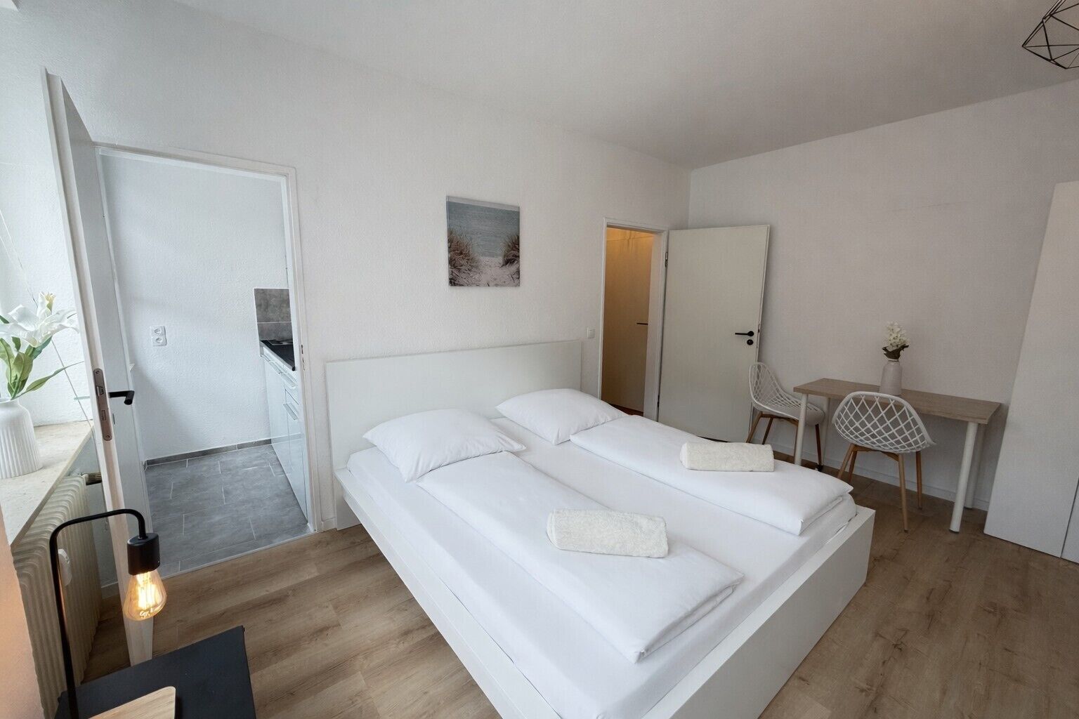 Ett sovrum med en säng, ett skrivbord, en stol och ett litet bord med en vas.