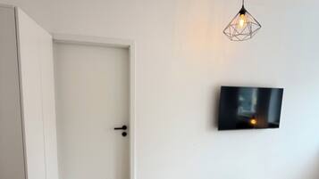 A bedroom with a bed, a TV mounted on the wall, a door, and a hanging light fixture.