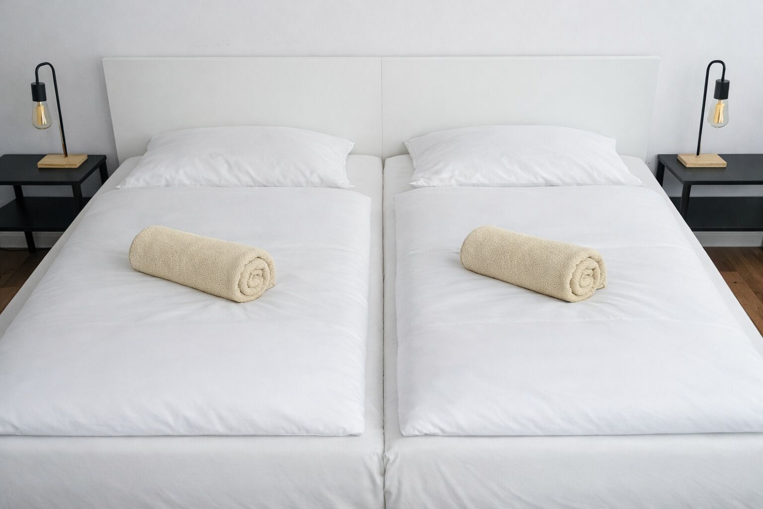 Ein Doppelbett mit weißen Bettwäsche und zwei aufgerollten Handtüchern, jeweils mit einem kleinen Nachttisch und einer Lampe.
