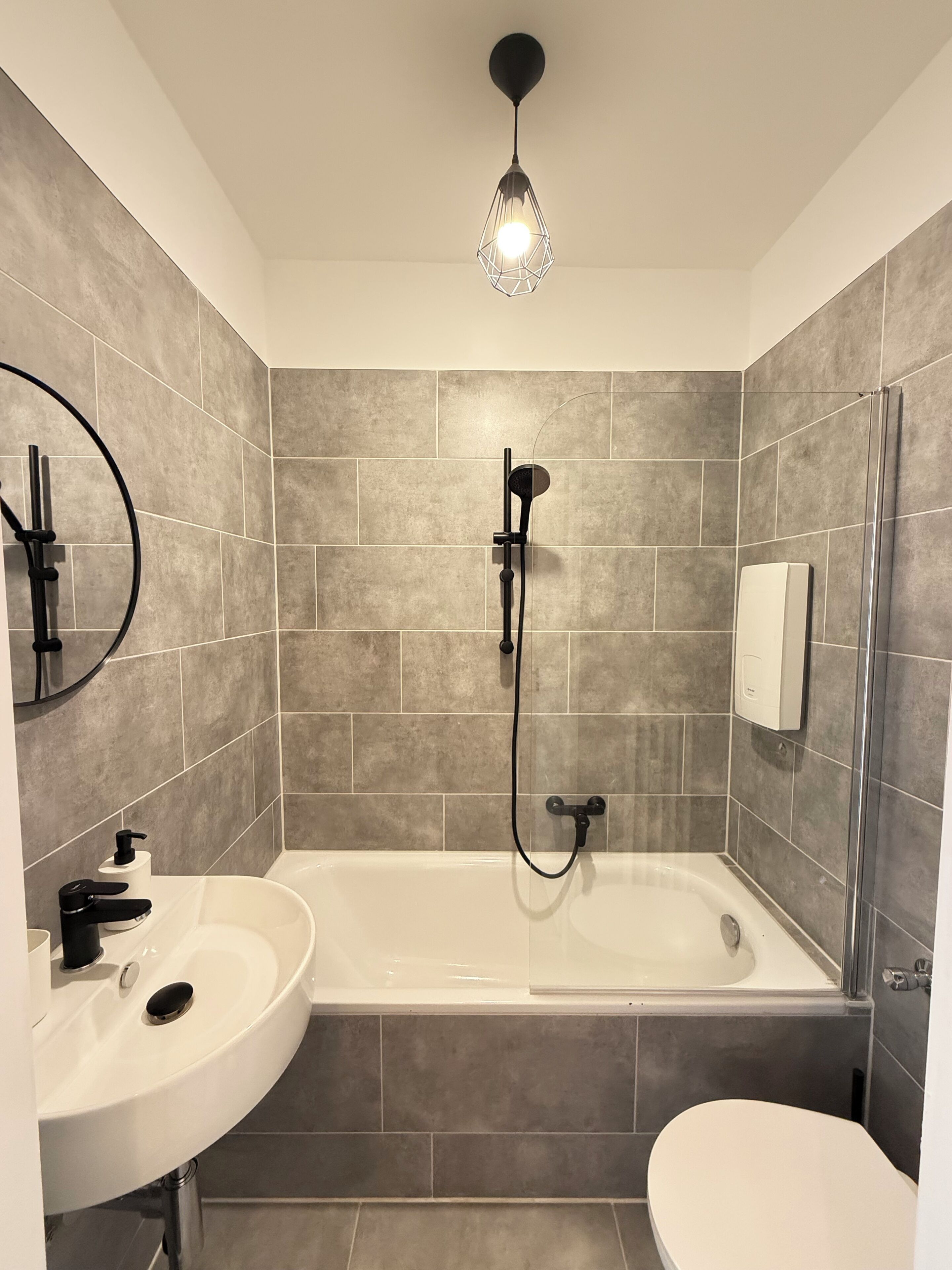 Une salle de bain moderne avec une baignoire sur pieds, un miroir rond et une douchette à main.