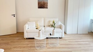 Un salón minimalista con un sofá blanco, dos mesitas auxiliares blancas y una puerta blanca.