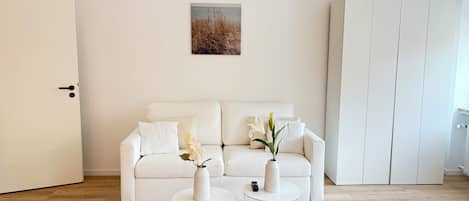 Un salón minimalista con un sofá blanco, dos mesitas auxiliares blancas y una puerta blanca.