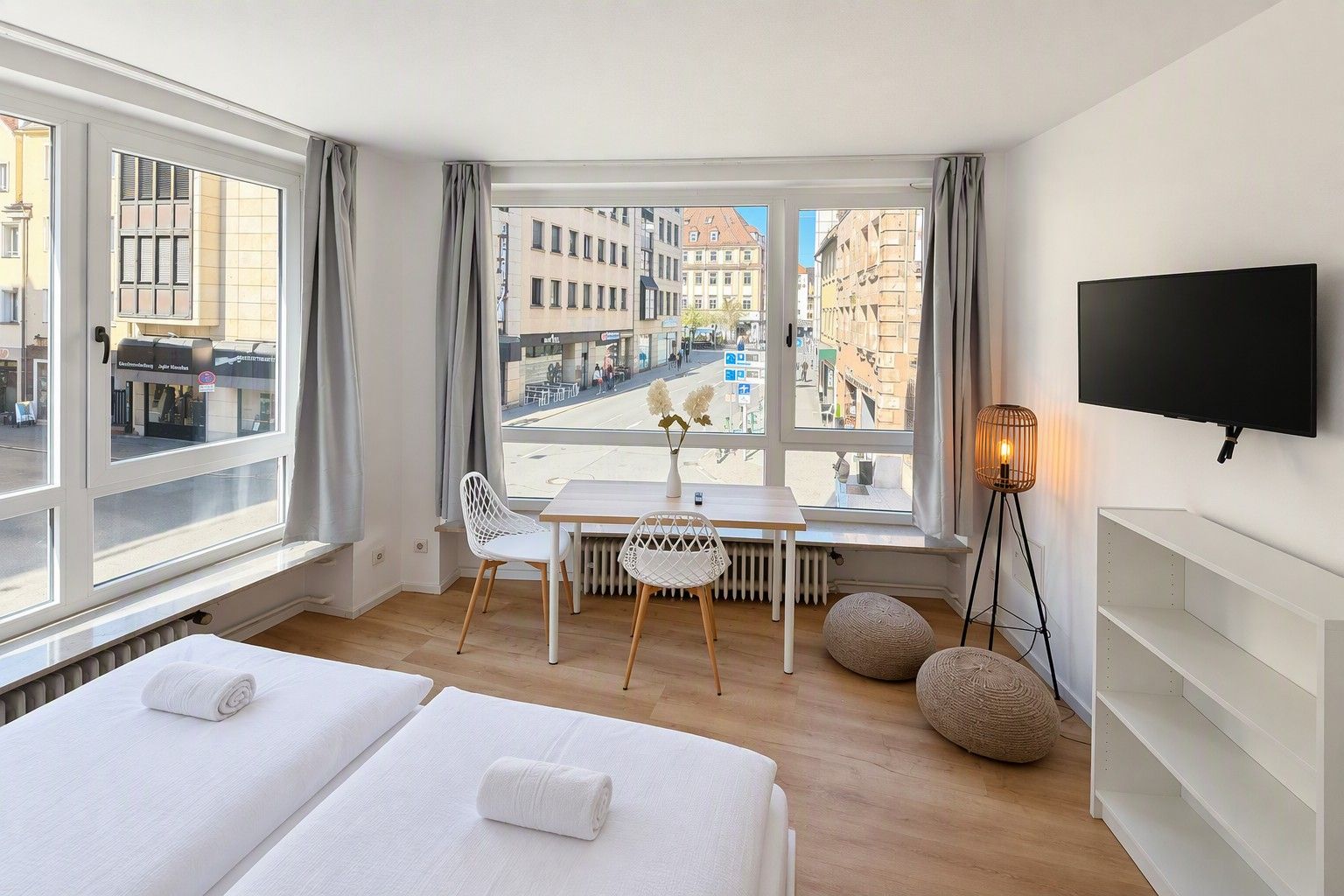 Ein Hotelzimmer mit zwei Betten, einem Esstisch, Stühlen, einem Fernseher und Blick auf die Stadt.