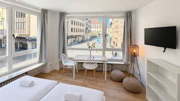 Ein Hotelzimmer mit zwei Betten, einem Esstisch, Stühlen, einem Fernseher und Blick auf die Stadt.