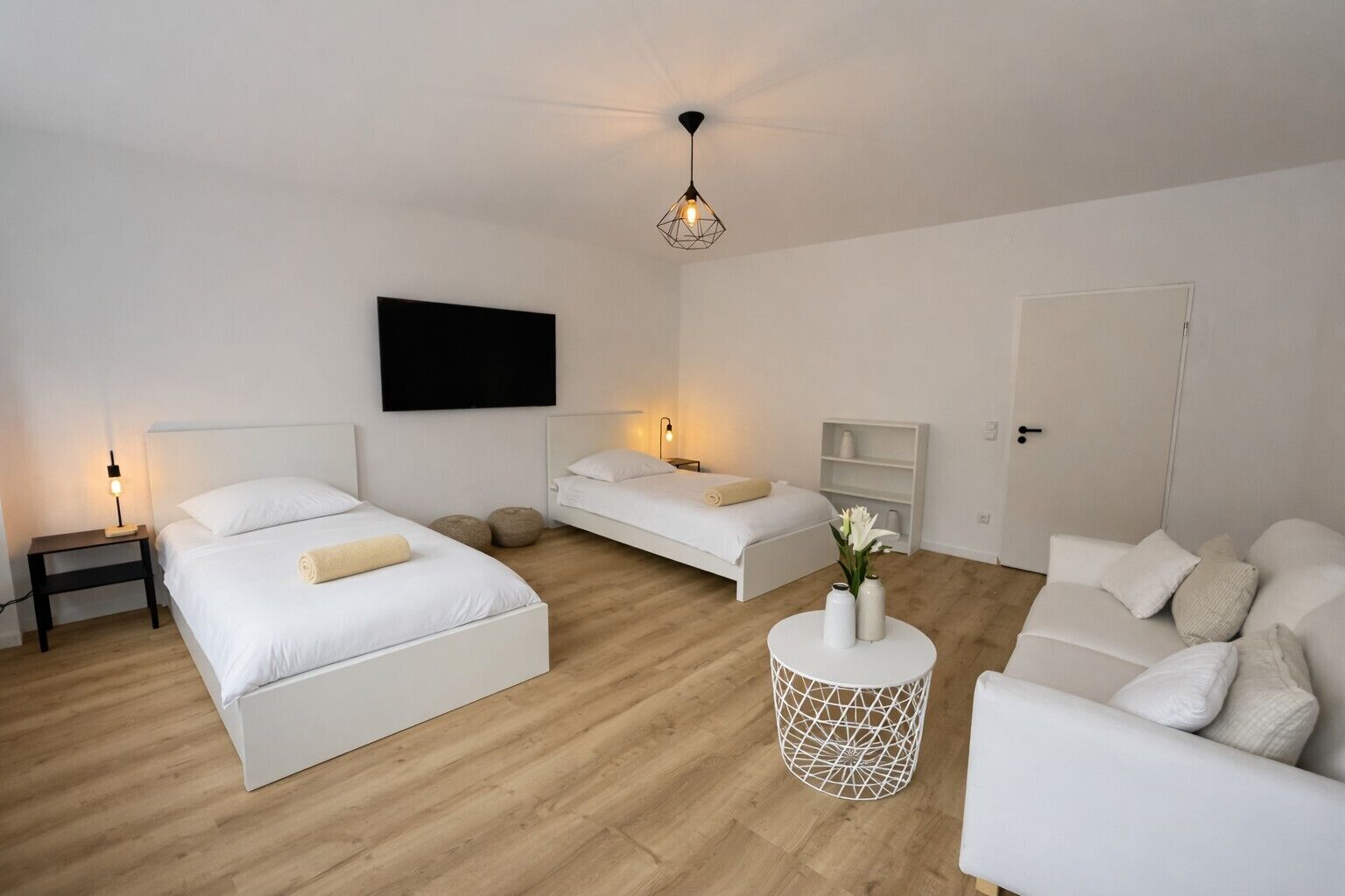 Ein schlicht eingerichtetes Schlafzimmer mit zwei Betten, einem Sofa, einem Fernseher und einem runden Beistelltisch.