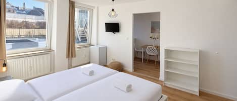 A hotel room with two beds, a TV, a radiator, a window with a view, and a small table with chairs.