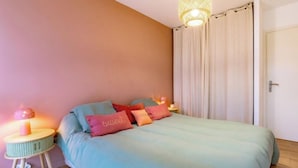 Un dormitorio con cama, almohadas, lámpara de noche y cortina.