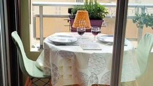 Un balcón con una mesa preparada para dos, una silla y una planta en maceta.
