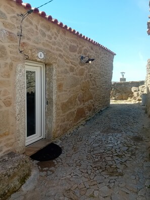 Un bâtiment en pierre avec un toit en tuiles, une porte et une cour dallée de pierres.
