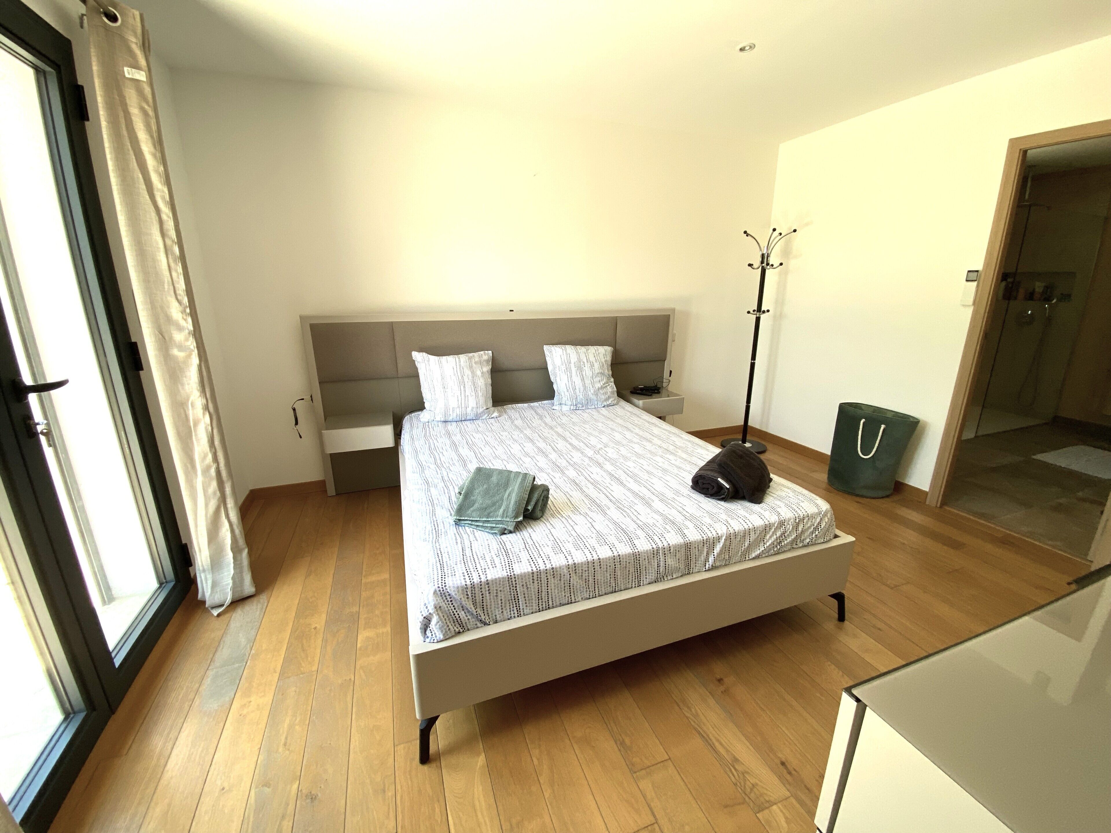 A modern bedroom with a bed, a bedside table, a floor lamp, and a view of a bathroom.