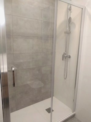 Een douche met glazen wand, een handdouche en een kraan op de muur.