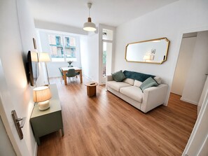 Ein modernes Wohnzimmer mit einer Couch, einem Esstisch mit Stühlen, einer Lampe und einem Spiegel an der Wand.