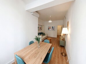 Een moderne woonkamer met een houten eettafel, teal stoelen, een bank en een lamp.