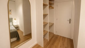 Una stanza con uno specchio grande, un armadio con ripiani multipli, un comodino con una lampada e una porta con maniglia.