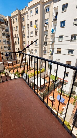 Ein Balkon mit Fliesenboden, einem Metallgeländer und Blick auf ein Wohngebäude mit zahlreichen Fenstern und Balkonen.