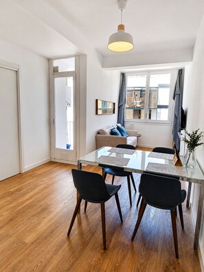 A dining area with a glass table, four chairs, a sofa, a window with curtains, and a hanging light fixture. - CC62 Apartamento Sagrada Familia de Barcelona (Barcelona)