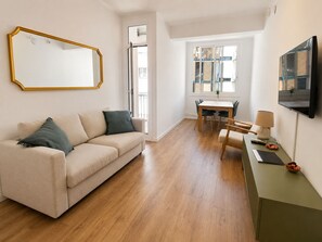 A modern living room with a sofa, a dining table, and a TV mounted on the wall. - CC52 Apartamento con balcón cerca Sagrada Familia (Barcelona)