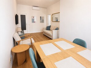 Ein möbliertes Zimmer mit einem Holztisch, zwei Stühlen, einem Sofa, einem Fernseher und einem Spiegel.