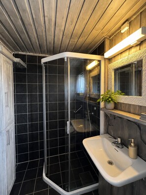 Ein modernes Badezimmer mit einer Duschkabine aus Glas, einem weißen Waschbecken und einer Holzwaschmöbel.'