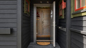 A narrow entrance with a wooden door, a red and green window trim, and a stone-tiled step.