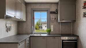A modern kitchen with grey cabinets, a built-in oven, and a window with a view of a house.