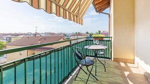 Un balcone con ringhiera verde, un tavolino con due sedie e vista sugli edifici vicini.