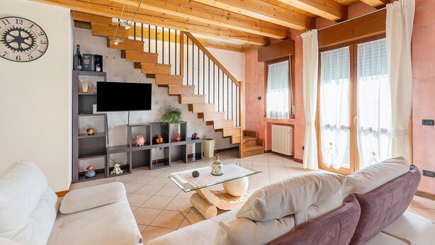 Un soggiorno con una scala in legno, una TV a schermo piatto, un divano e un tavolino da caffè.