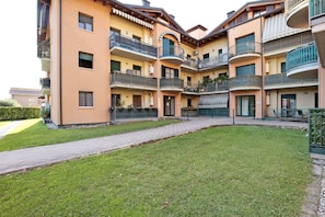 Un immeuble résidentiel à plusieurs étages, doté de balcons, d’une allée pavée et d’une pelouse bien entretenue.