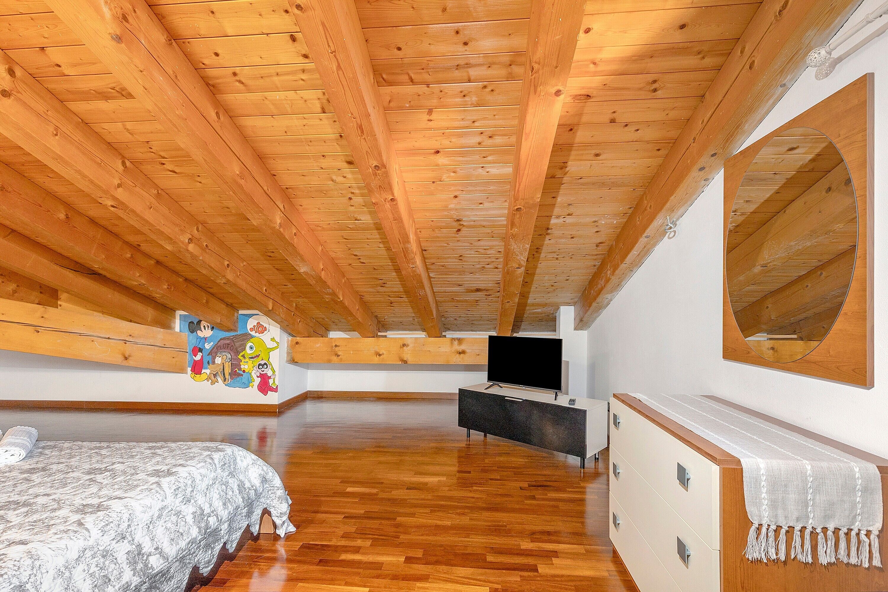 Ruime kamer met houten plafond, een bed, een dressoir, een televisie en een grote spiegel.