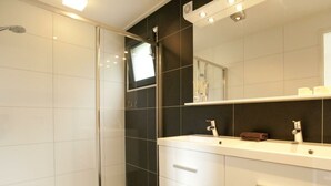 A modern bathroom with a glass shower enclosure, a white vanity with a mirror, and dark tiled walls. - Cube Magnifique 8 (Nijkerk)