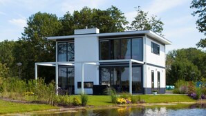 A modern two-story house with large windows, a flat roof, and a pond in the foreground. - Cube Magnifique 8 (Nijkerk)