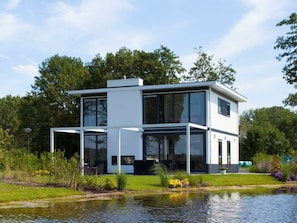 Ein modernes, zweistöckiges Haus mit großen Fenstern, einer flachen Dachkonstruktion und einem Teich im Vordergrund.