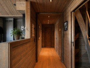 A wooden hallway with a staircase, a potted plant, and a wall-mounted sign.