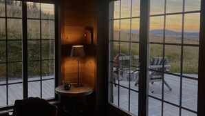 Ett rum med stora fönster, en lampa, en stol och ett litet bord.