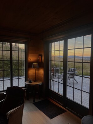A room with large windows, a lamp, a chair, and a small table.