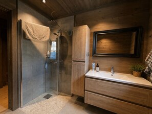 Ein modernes Badezimmer mit einer Duschkabine aus Glas, Holzschränken und einem großen Spiegel.
