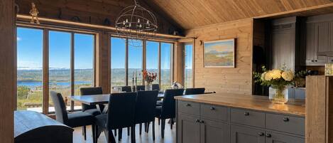 A dining area with a view of a lake, wooden ceiling, and a chandelier.