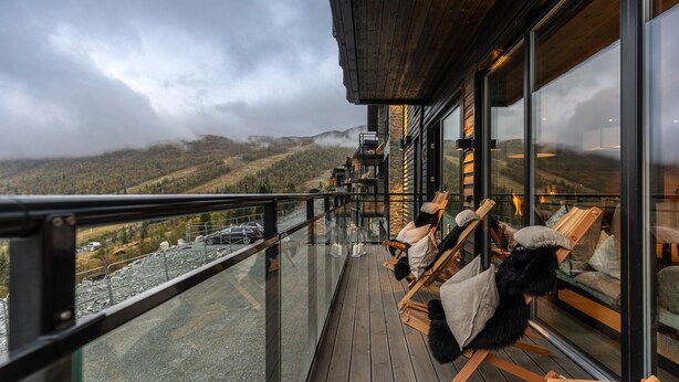 Un balcón con sillas y cojines de madera, con vistas a un paisaje montañoso.